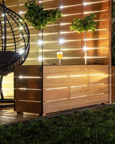 Residential Backyard Garden Wooden Recreation Place Deck with Table Illuminated by LED Outdoor Lighting. Custom Made Wooden Element.